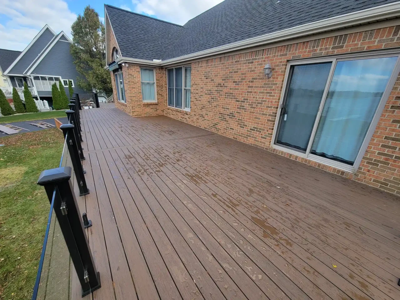 A large brown composite deck with black railing attached to a brick house with sliding glass doors.