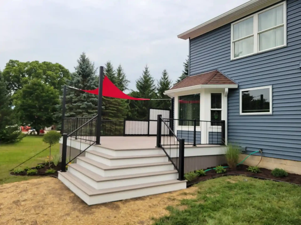 Elevated deck viewed from the right side, featuring wide white steps, black metal railing, and a red triangular shade sail.