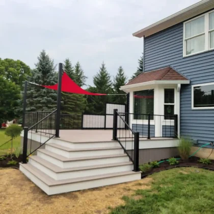 Elevated deck viewed from the right side, featuring wide white steps, black metal railing, and a red triangular shade sail.