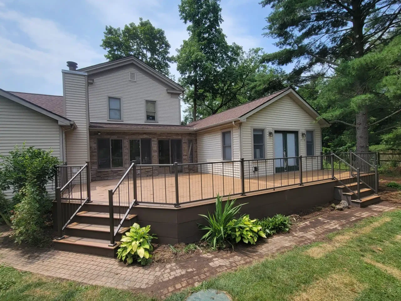 Elevated composite deck with brown tones, black cable railing, and wide steps, attached to a beige house with a tiki bar room