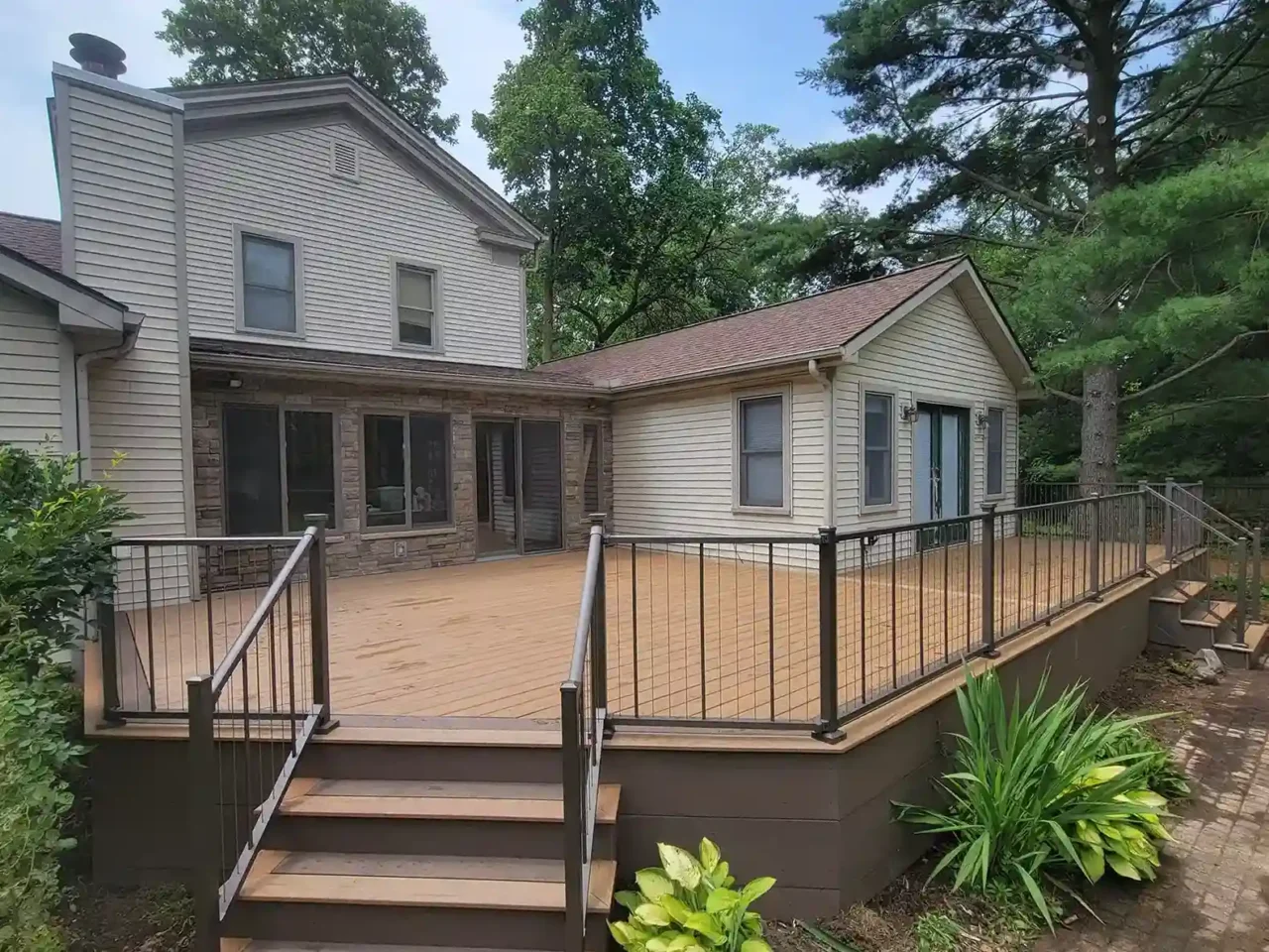 Elevated composite deck with TimberTech Antique Leather decking, Dark Cocoa accents, and black cable railing, viewed from the front right, attached to a beige house.