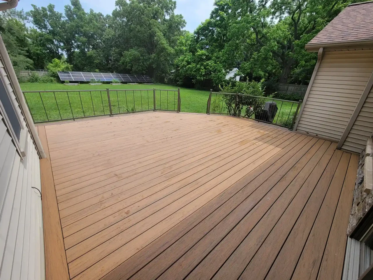Composite deck with TimberTech Antique Leather boards and black cable railing, overlooking a grassy yard with solar panels.