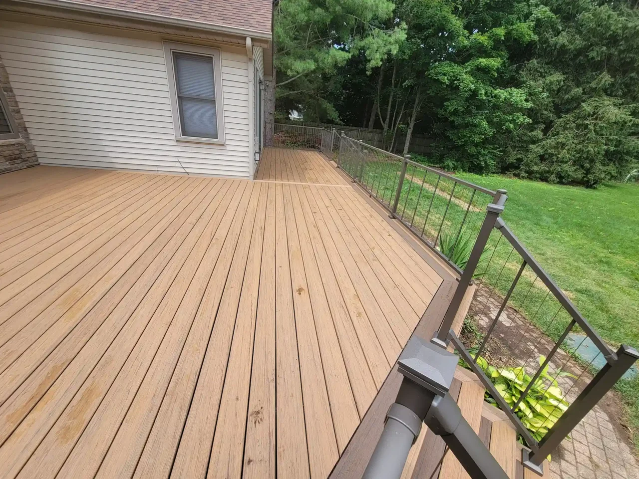 Composite deck with TimberTech Antique Leather boards and black cable railing, viewed from the top of the staircase, overlooking a green yard.