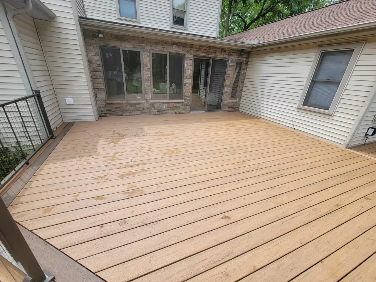 Composite deck with TimberTech Antique Leather boards, bordered by black cable railing, attached to a beige house with stone accents and large windows.