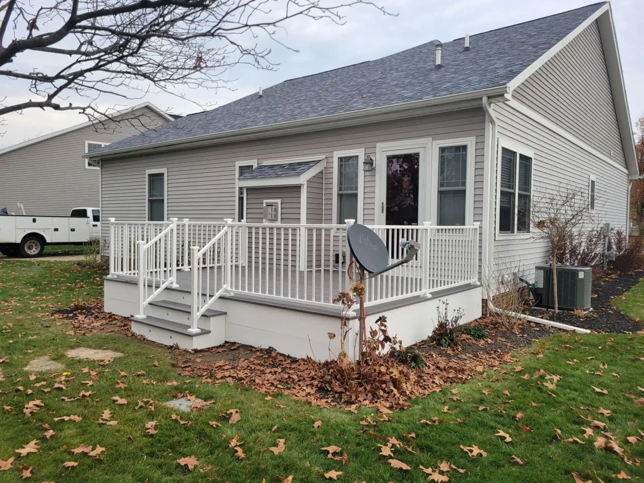 A white-railed deck with stairs leading to a backyard beside a gray house on a cloudy day.