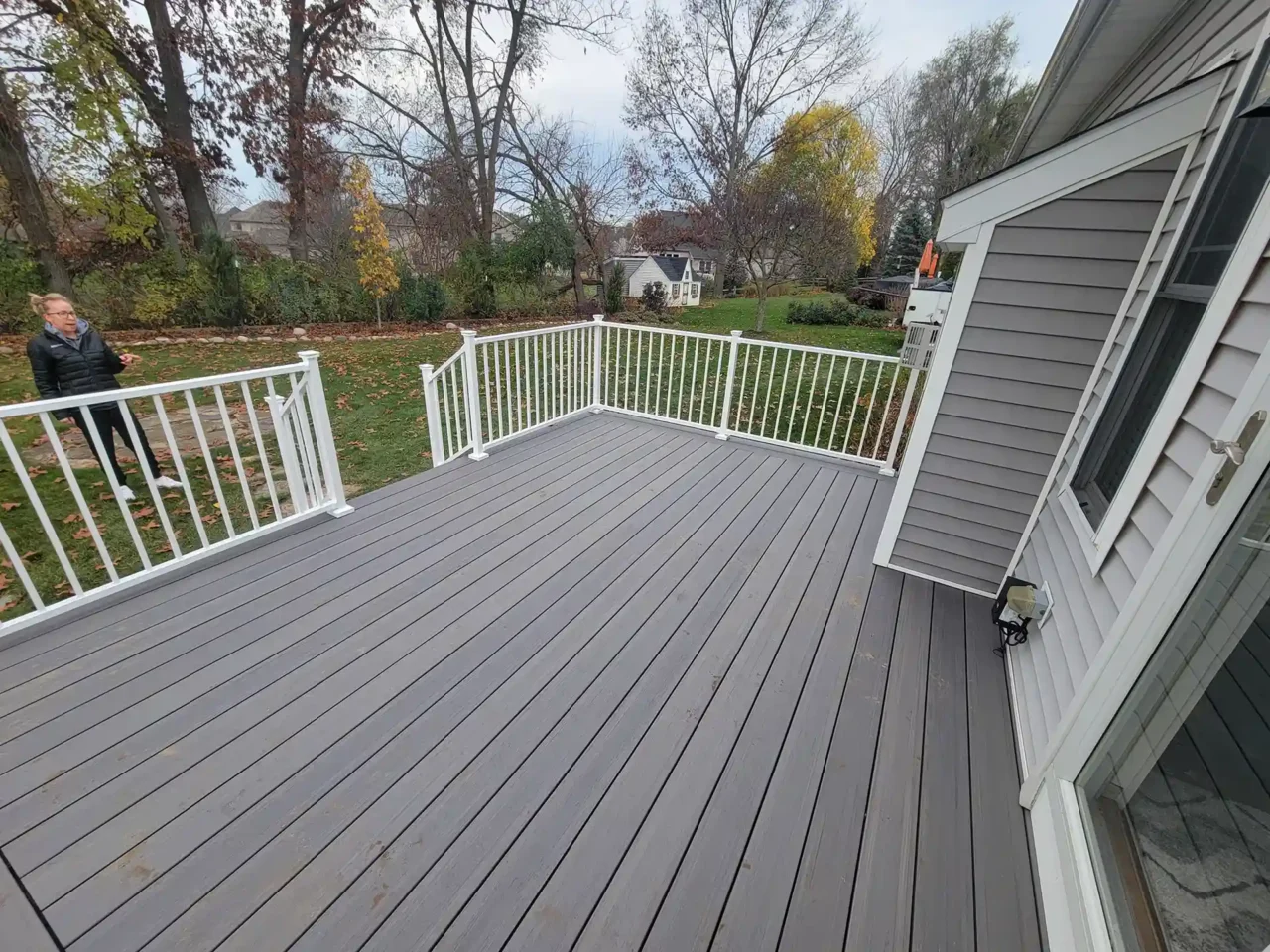 A gray PVC deck floor with white railings overlooking a backyard with trees and grass.