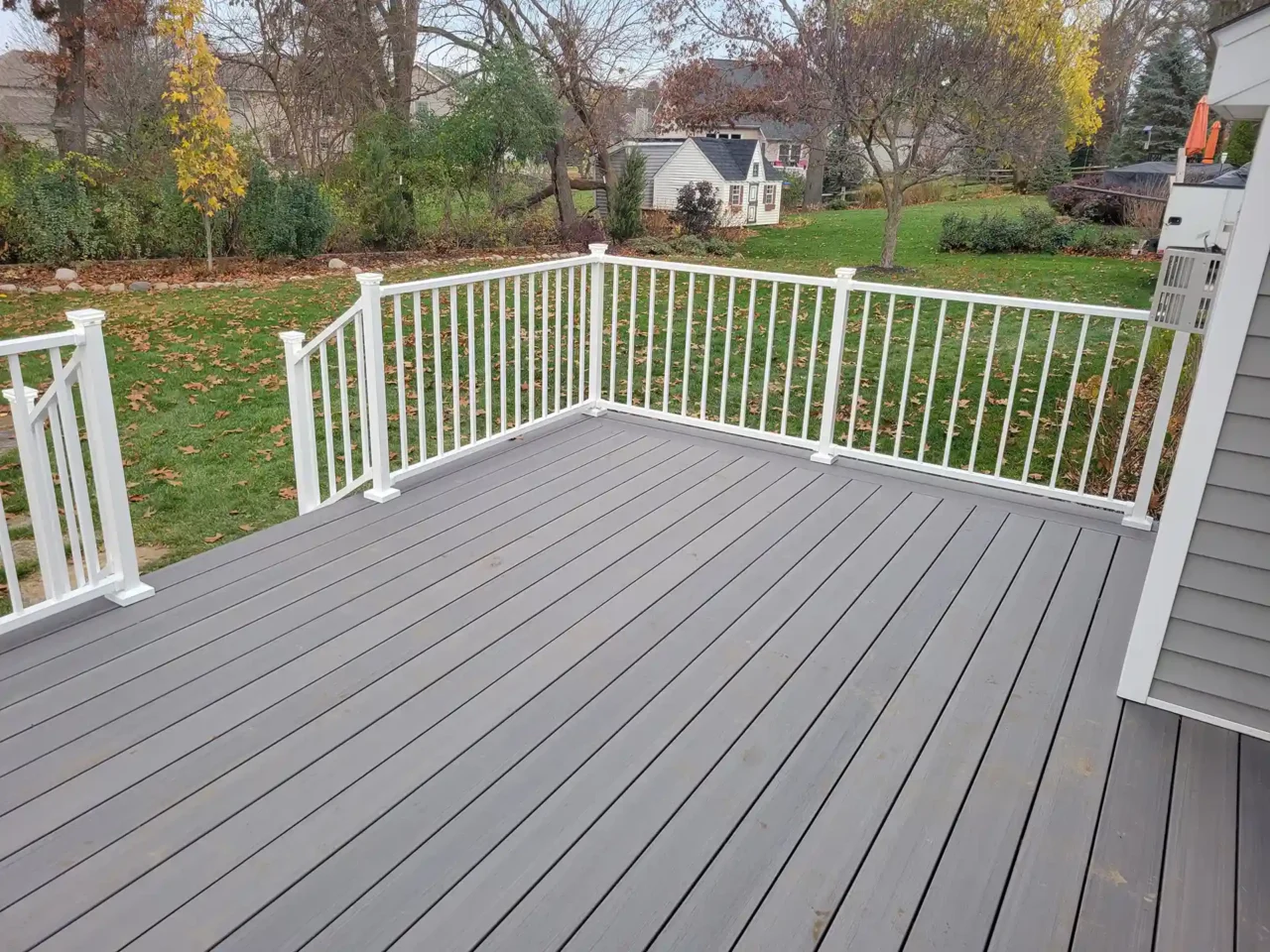 A gray PVC deck floor with white railings overlooking a backyard with trees and grass.