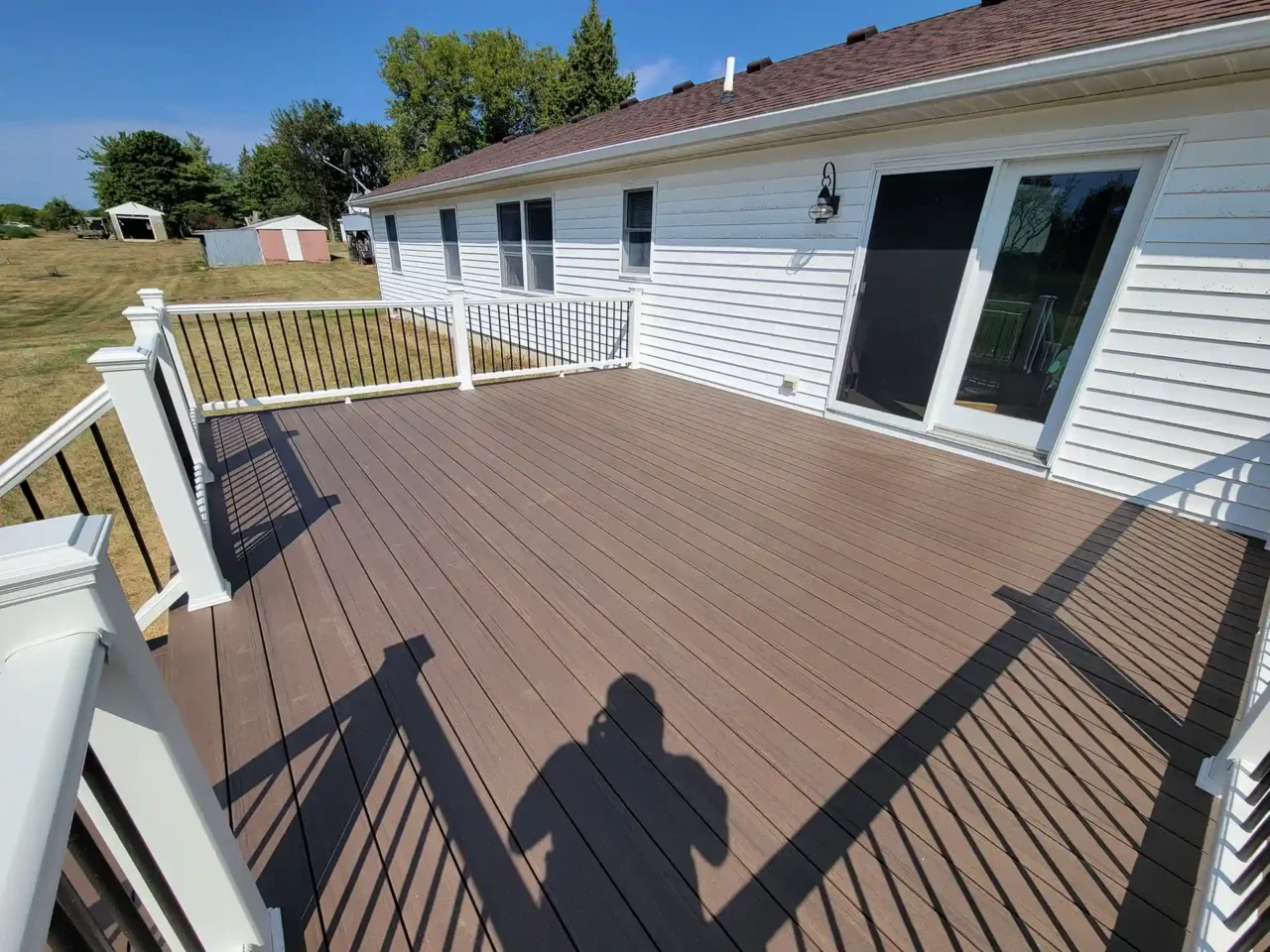 Spacious brown composite deck with white railing and black balusters attached to a white house, with sliding glass doors.