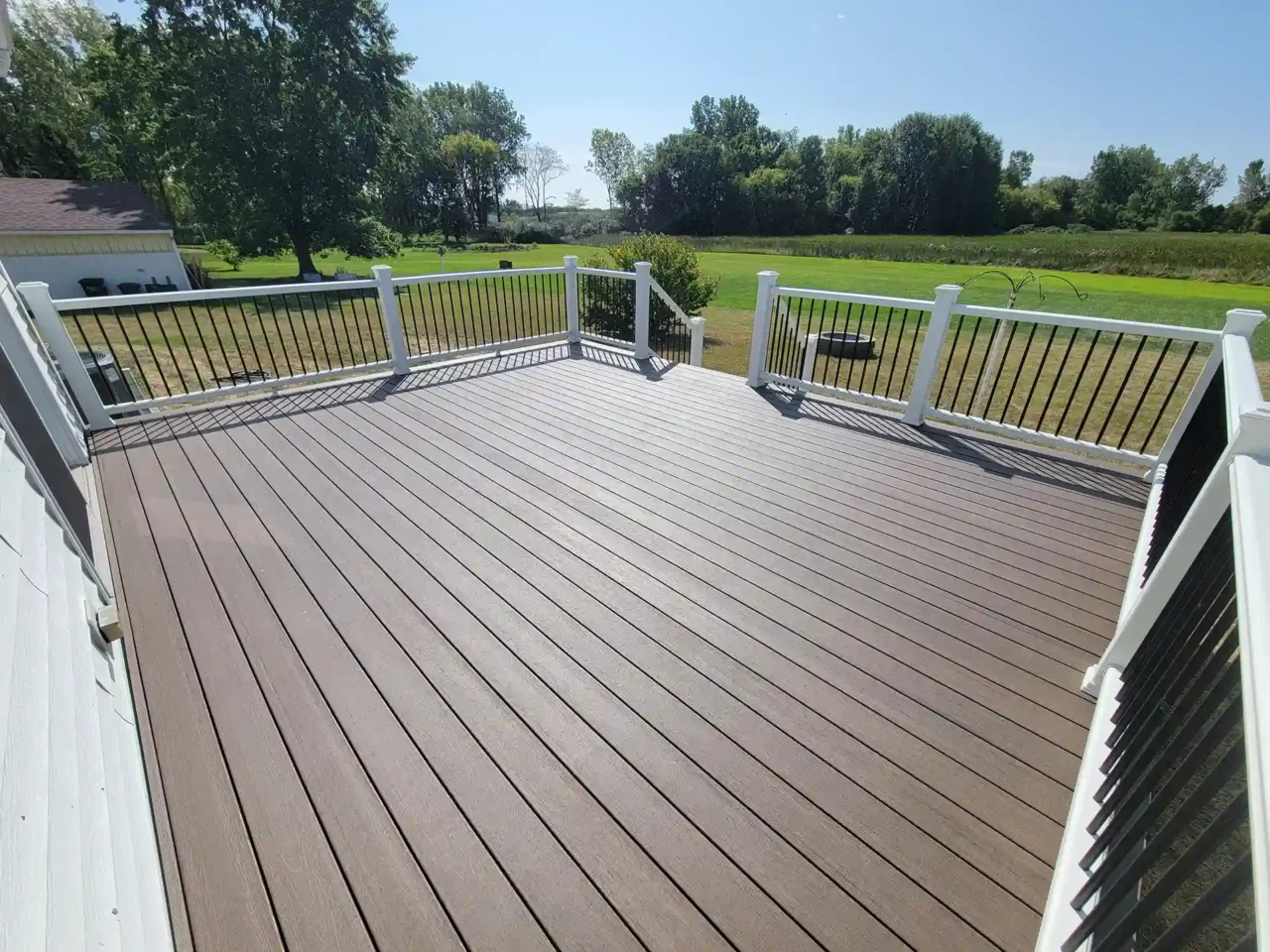 Spacious composite deck with white railing and black balusters attached to a white house, overlooking a large grassy yard.